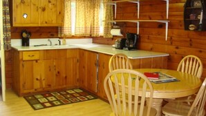 A compact kitchen with wooden cabinets, a sink, and a dining area with a table and chairs. - On North Twin Lake- Northern Exposure Rentals "Minnow Bucket" (Phelps)