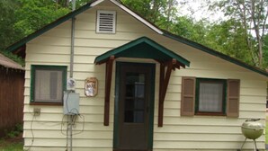 A small, single-story house with a green door and shutters, a small porch, and a barbecue grill in the yard. - On North Twin Lake- Northern Exposure Rentals "Minnow Bucket" (Phelps)