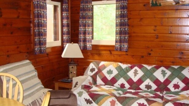 A cabin room with a bed, a chair, a table, and a window with curtains. - On North Twin Lake- Northern Exposure Rentals "Minnow Bucket" (Phelps)