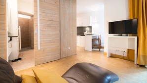 A modern living room with a sliding wooden door, a flat-screen TV on a white stand, and a sofa with cushions. - Vienna Residence, City Hall - Parliament #6408 (Vienna)