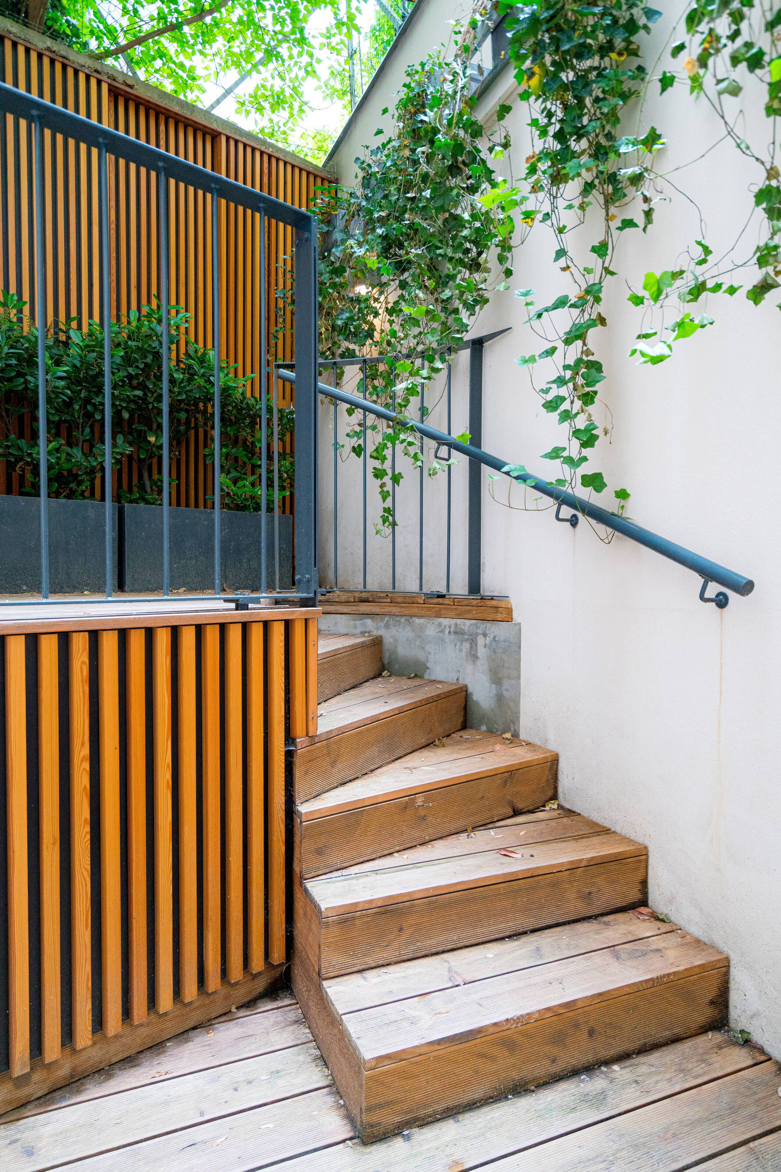 A wooden staircase with a metal handrail, leading to a balcony with vertical wooden slats and a view of greenery.