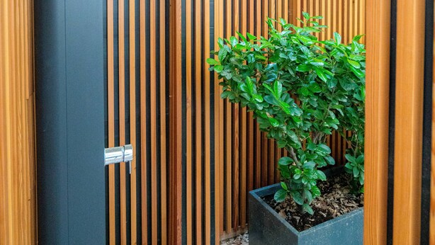A wooden fence with vertical slats, a planter box with a shrub, and a metal gate. - Vienna Residence, City Hall - Parliament #6408 (Vienna)