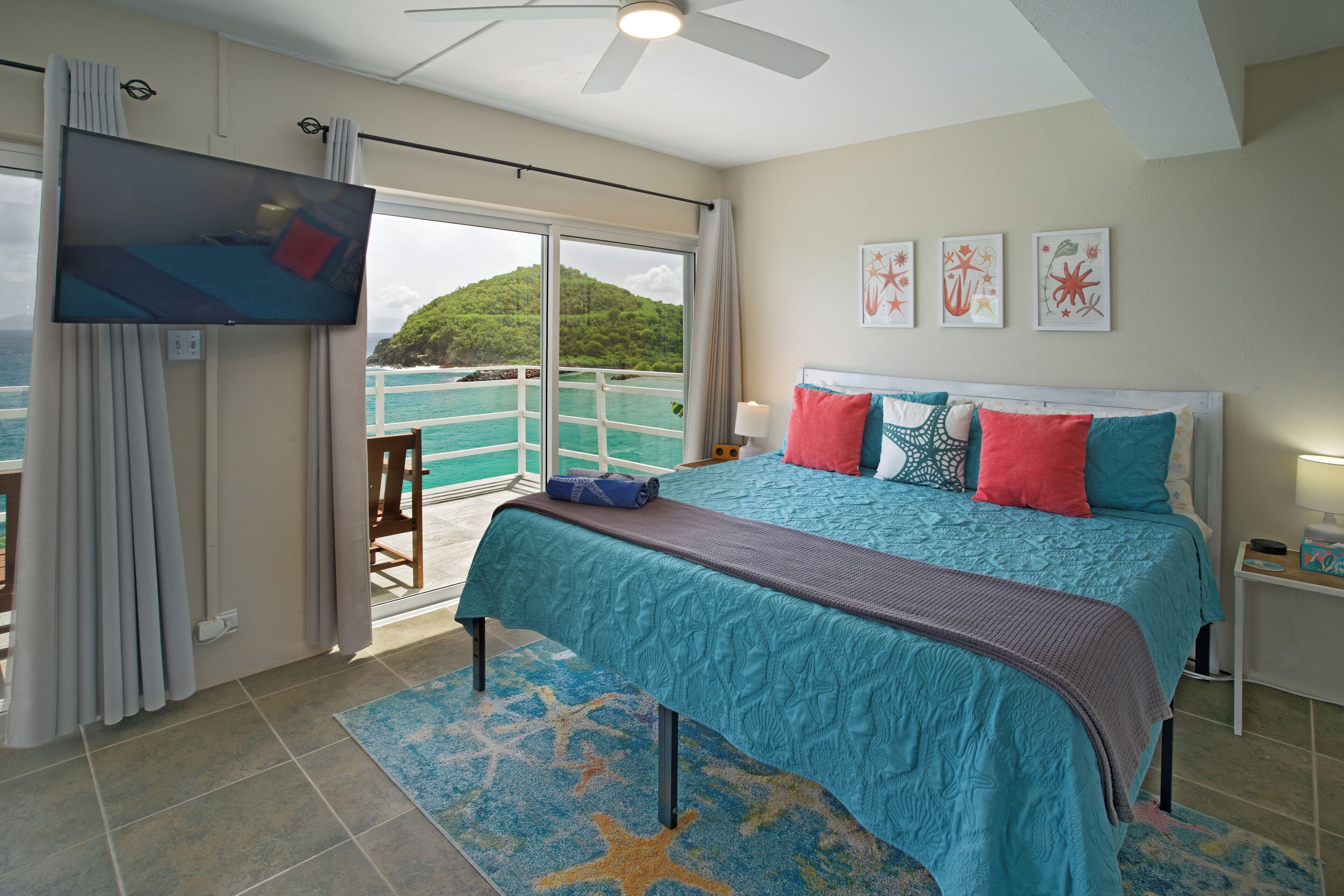Une chambre avec un lit, une télévision, un balcon donnant sur la mer et des œuvres d’art accrochées au mur.
