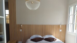 Een slaapkamer met een bed, een houten latten hoofdbord, een hanglamp en een raam met jaloezieën.