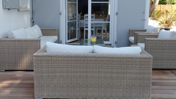 Een terras met rieten meubilair en een glazen deur naar een binnenruimte.