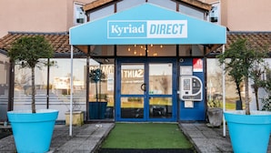 Un bâtiment avec une enseigne bleue portant l’inscription « Kyriad DIRECT » au-dessus de l’entrée.