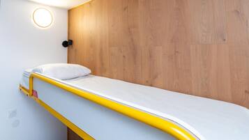 Een stapelbed met een witte matras en geel frame, een houten wand en een ronde lamp.