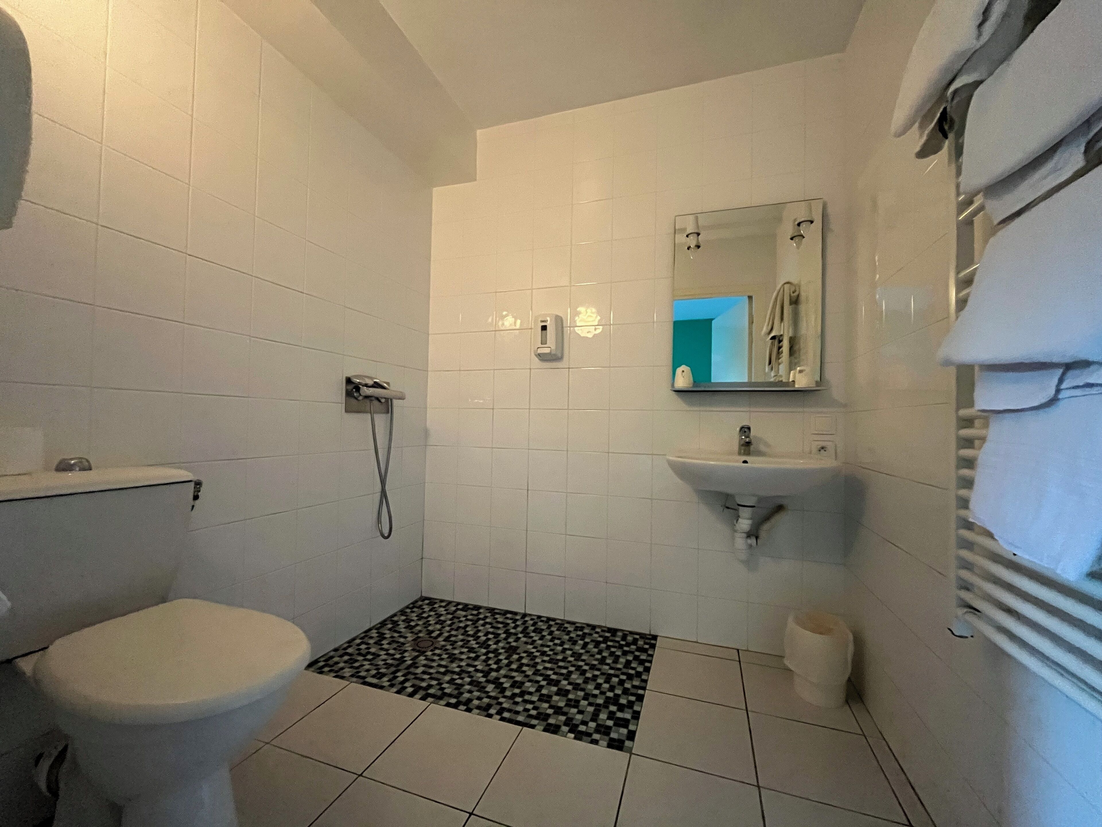 Un baño con inodoro, ducha, lavabo y suelo de baldosas con diseño a cuadros blanco y negro.