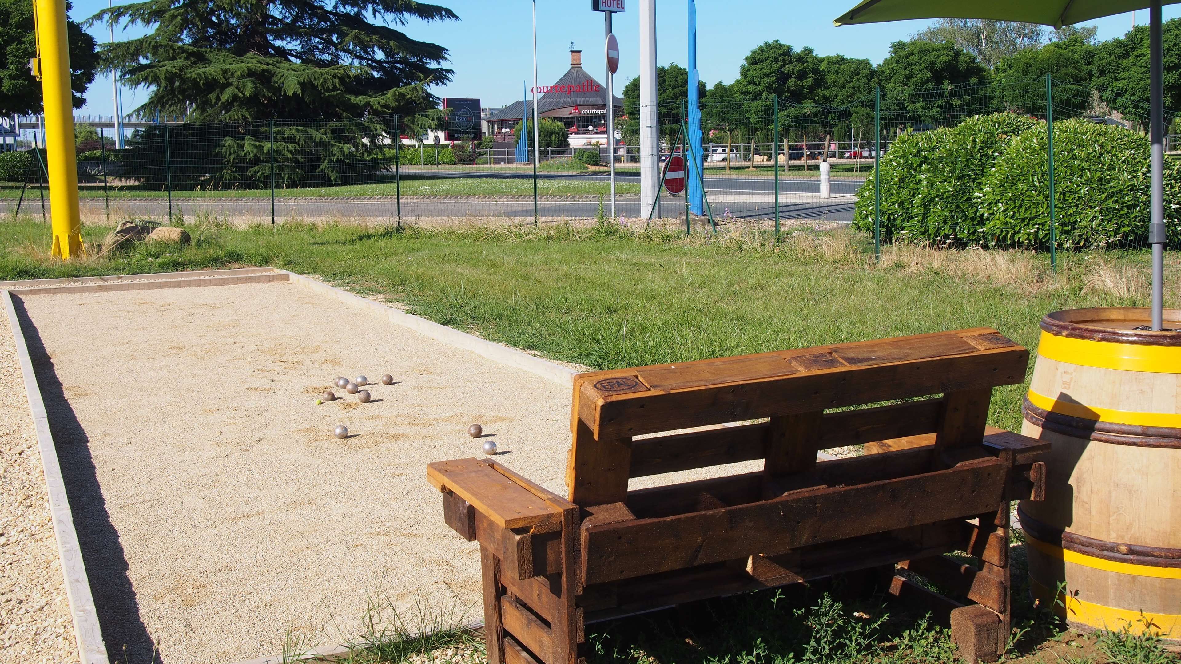 Un banc en bois dans un parc, avec une zone recouverte de gravier et un poteau jaune à proximité.