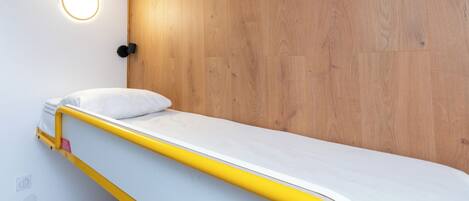 A bunk bed with a yellow frame and white mattress, a wooden panel wall, and a circular light fixture above the bed.