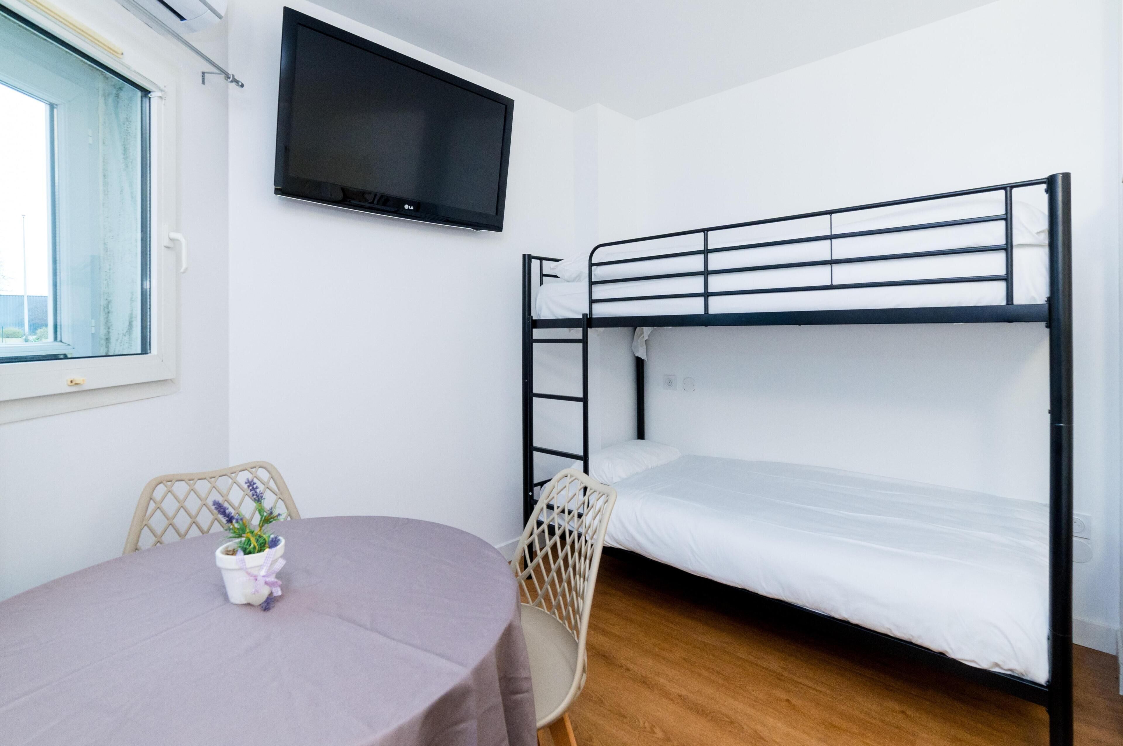 A bunk bed room with a TV, a table with a chair, and a window.