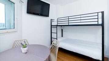 A bunk bed room with a TV, a table with a chair, and a window.