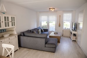 Un espacio habitable pequeño con un sofá gris, muebles de cocina blancos y un televisor.