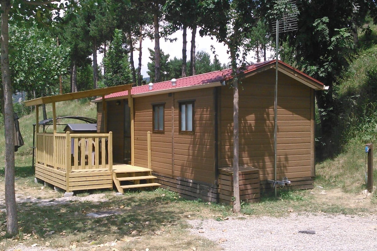 Uma pequena cabana de madeira com varanda, telhado vermelho e chaminé.