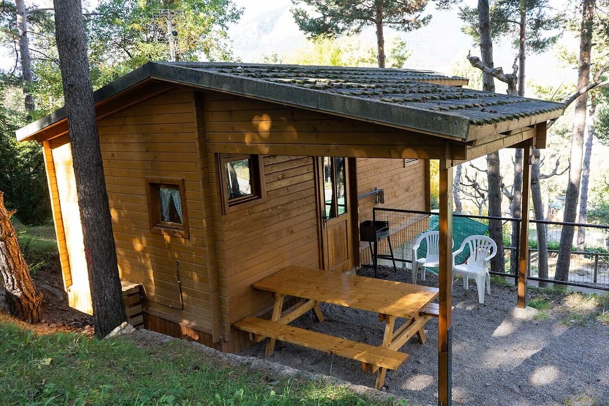Uma pequena cabana de madeira com varanda, um banco e duas cadeiras.