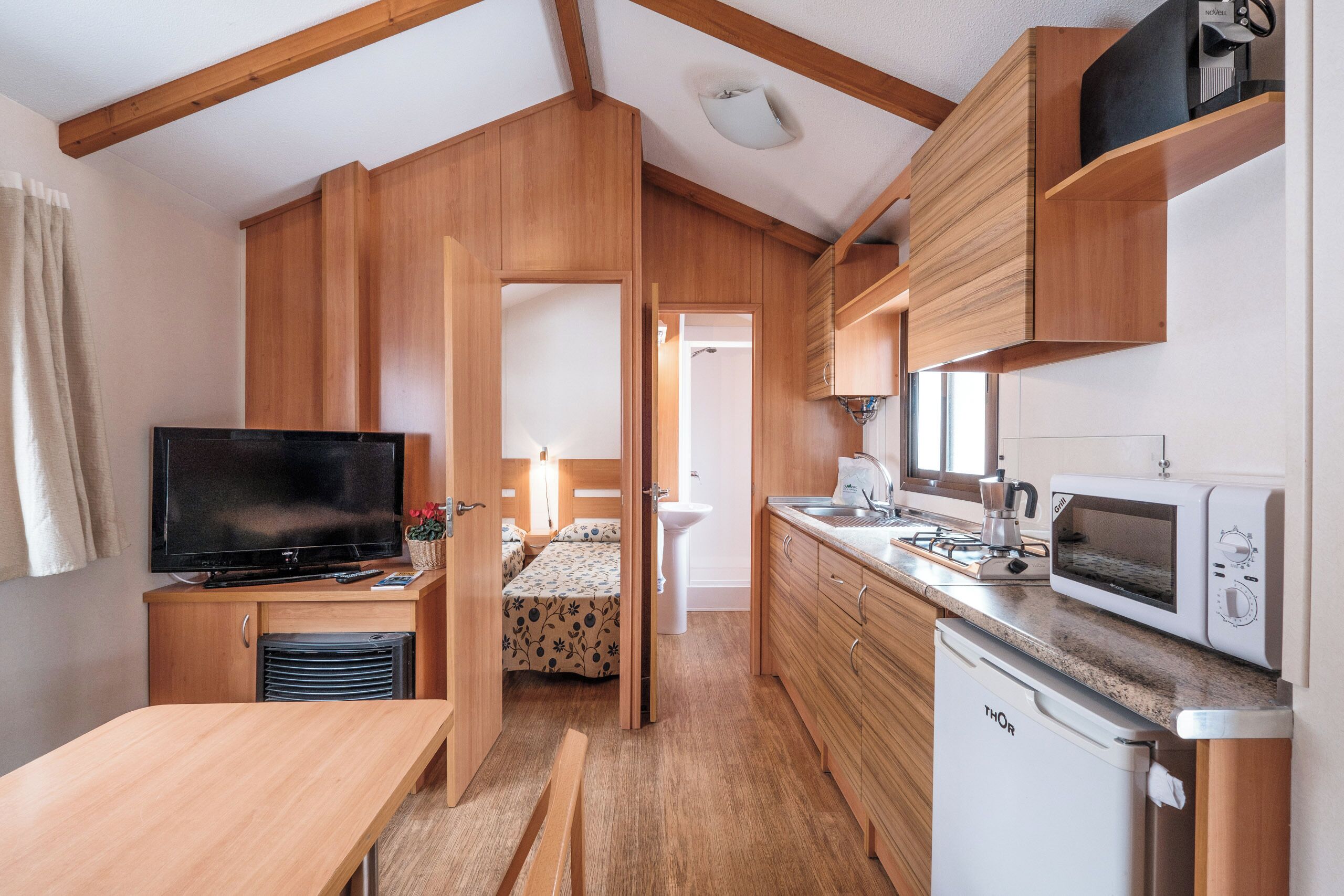 A compact kitchen with wooden cabinets, a microwave, a coffee maker, and a dishwasher.