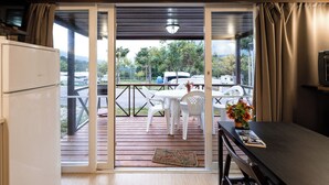 Une pièce dotée d’une porte-fenêtre coulissante donnant sur une terrasse extérieure avec une table et des chaises, un réfrigérateur et une petite table sur laquelle est posé un vase de fleurs.