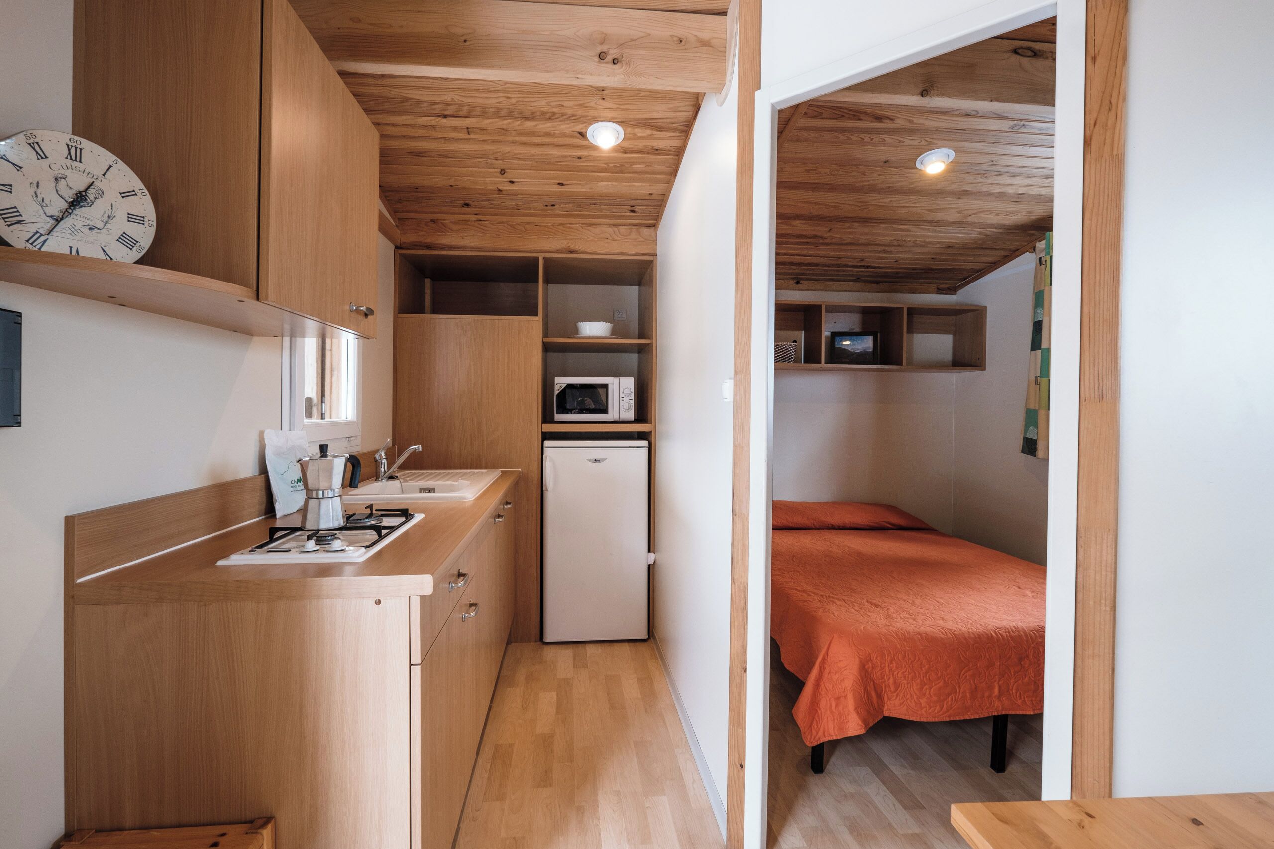 Una cocina compacta con armarios de madera, un microondas y un refrigerador pequeño.