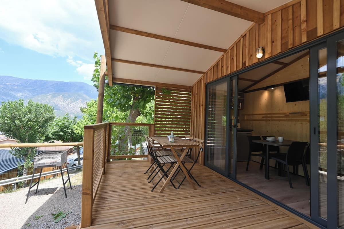 Um deck de madeira com mesa e cadeiras, uma porta de vidro deslizante que dá para uma cozinha e vista para montanhas.