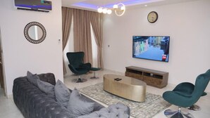 A modern living room with a grey tufted sofa, a green armchair, a coffee table, and a TV mounted on the wall. - Luxury House - Sleeps 8 & Free Parking (Abuja)