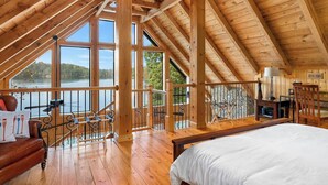 Een chalet met een slaapkamer op een entresol, een balkon met uitzicht op een meer en een eethoek met een tafel en stoelen.
