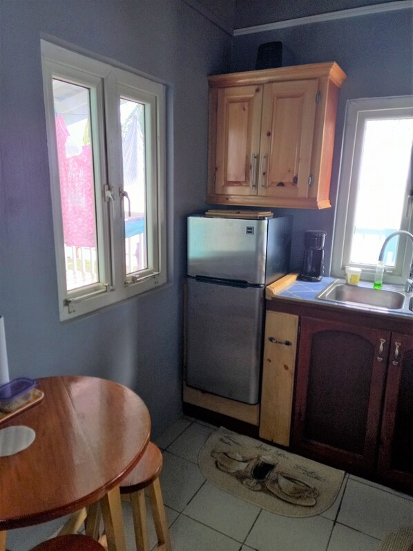 A compact kitchen with wooden cabinets, a stainless steel refrigerator, a coffee maker, and a dining table with chairs. - idyllic, caribbean house with A/C right by the sea (Calibishie)