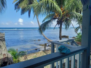 A wooden deck with a railing overlooking a beach with palm trees and the ocean. - idyllic, caribbean house with A/C right by the sea (Calibishie)