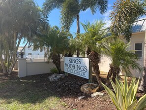 Skilt for 'Kings Moorings Condominium' med udsigt til en hvid bygning og palmer.