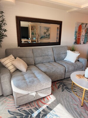 A grey sectional sofa with a footstool, a round coffee table with a gold base, and a patterned rug. - Cozy 1 Bedroom by the Skyway Marina District (St. Petersburg)