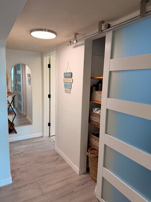 A hallway with a sliding door leading to a storage area, a mirror reflecting the hallway, and a sign with words 'GETAWAY,' 'SEA THE DAY,' 'SERENITY,' and 'RELAX.' - Cozy 1 Bedroom by the Skyway Marina District (St. Petersburg)