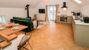 Una cocina moderna con horno empotrado, un área de comedor con sofá verde y un amplio ventanal con vistas a una terraza.