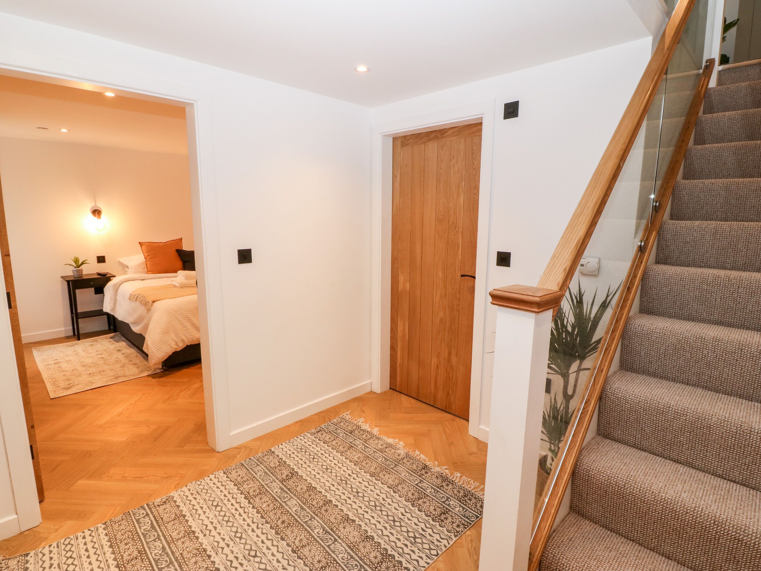 Un pasillo con una puerta de madera, una escalera con escalones alfombrados y una cama con un tapete estampado en la habitación contigua.