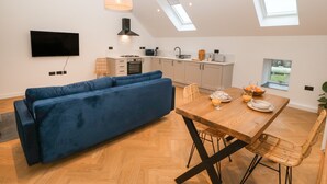 Una cocina moderna con comedor, que incluye un sofá azul, una mesa de comedor de madera y un televisor montado en la pared.
