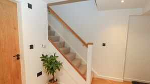 Una escalera con barandillas de madera y peldaños alfombrados, que conduce a un piso superior. Una planta en maceta se encuentra cerca de la base de la escalera.