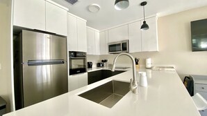 A modern kitchen with white cabinets, stainless steel appliances, a black countertop, and a built-in oven.