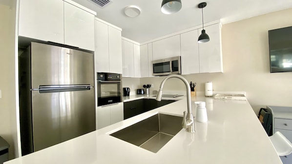 A modern kitchen with white cabinets, stainless steel appliances, a black countertop, and a built-in oven.