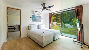A bedroom with two beds, a ceiling fan, and a large sliding glass door leading to a garden. - A luxury, modern and stylish sea view villa - 400 meters to the beach (Koh Phangan)