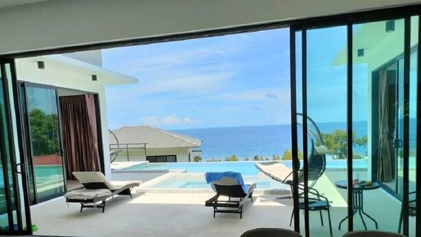 A modern room with a large sliding glass door leading to a pool area with lounge chairs and a view of the ocean. - A luxury, modern and stylish sea view villa - 400 meters to the beach (Koh Phangan)