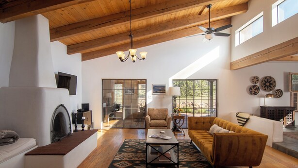 A spacious living room with a high ceiling, wooden beams, a fireplace, a sofa, a coffee table, and a view of the outdoors. - Sunlit 3 bedroom, enclosed dog friendly yard in quiet neighborhood (Santa Fe)