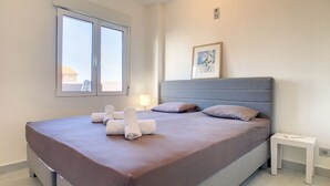 Une chambre à coucher avec un grand lit, une table de chevet, une fenêtre et un tableau encadré au mur.