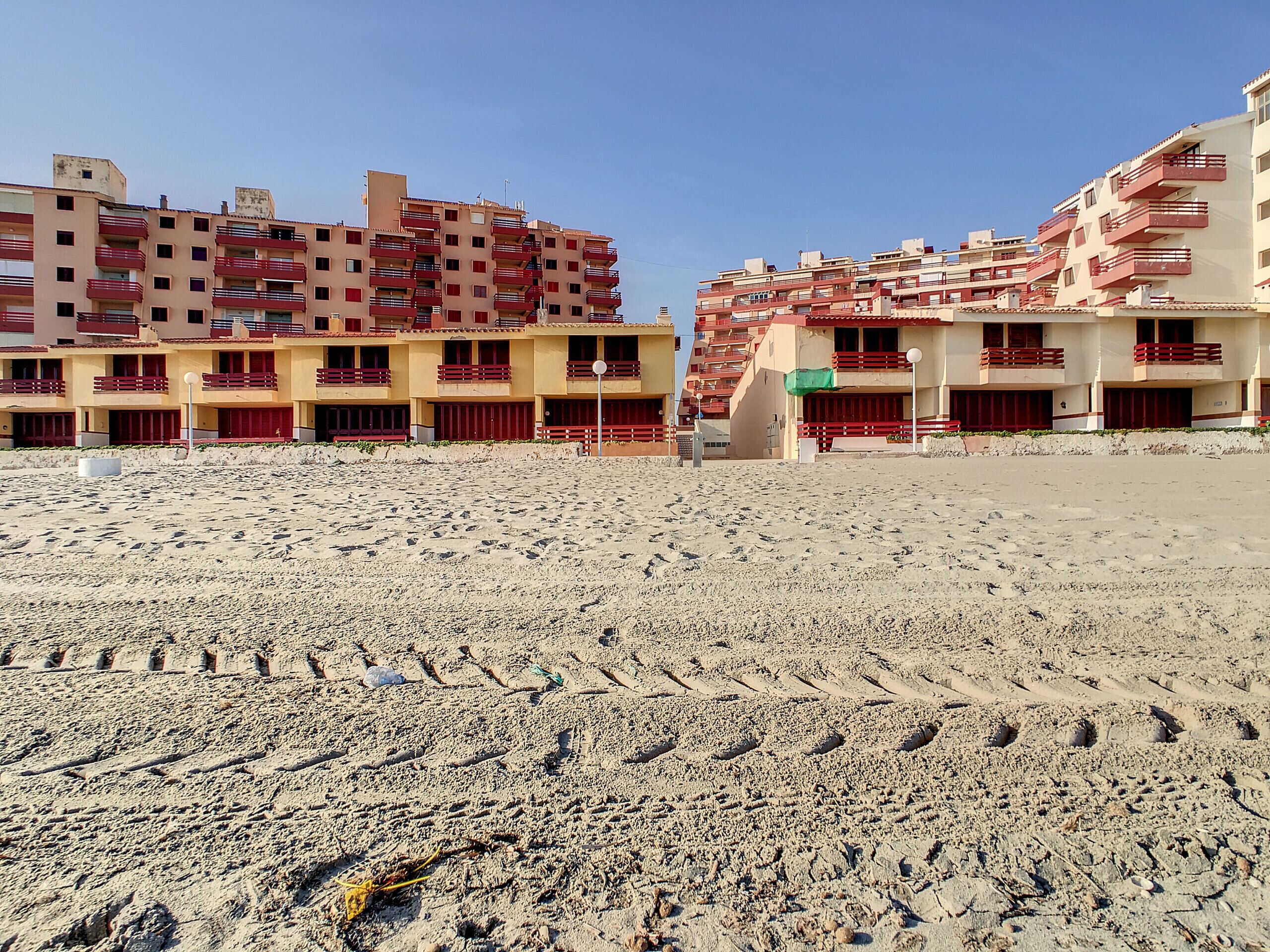 Een zandstrand met voetafdrukken die leiden naar een rij meerverdiepingen met balkons.