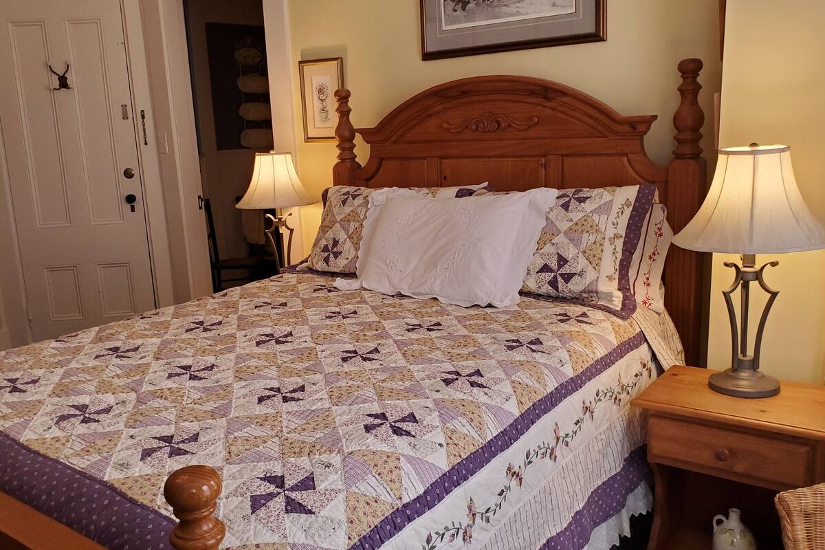 A neatly made bed with a patterned quilt, two bedside lamps, and a wooden headboard.