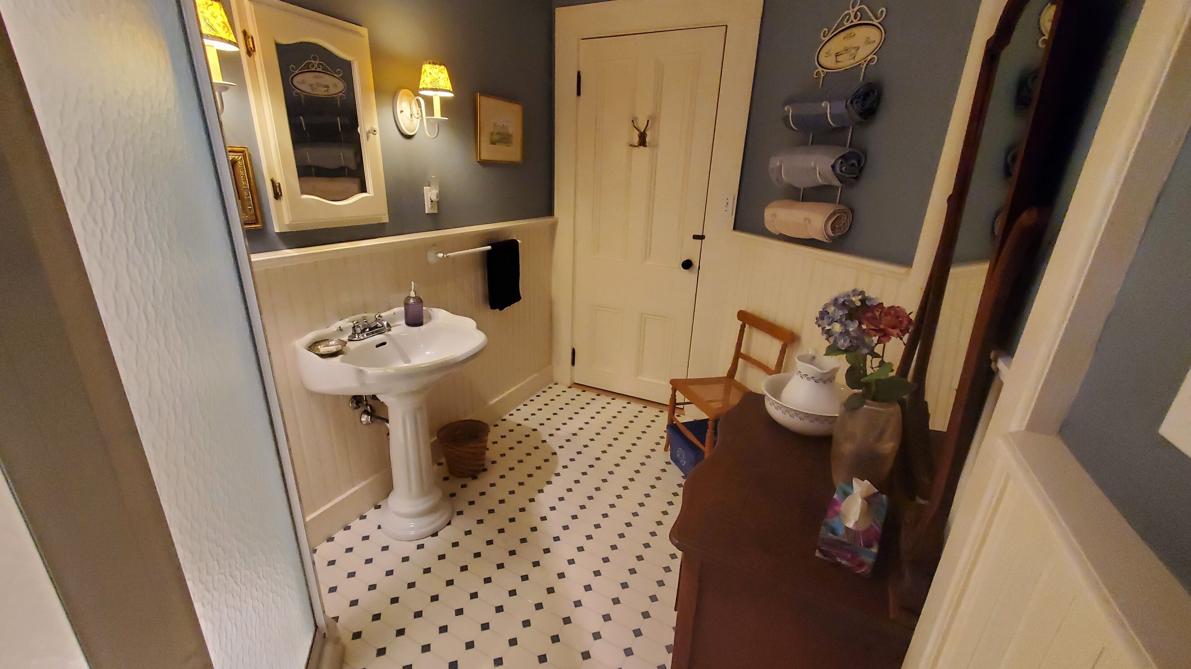 A bathroom with a white sink, a mirror, a towel rack, a door, and a patterned floor.