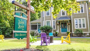 A sign for 'The Lark & Loon Inn' with a 'Bed & Breakfast' label, outdoor seating with chairs, and a house in the background. - The Lark & Loon Inn (Annapolis Royal)