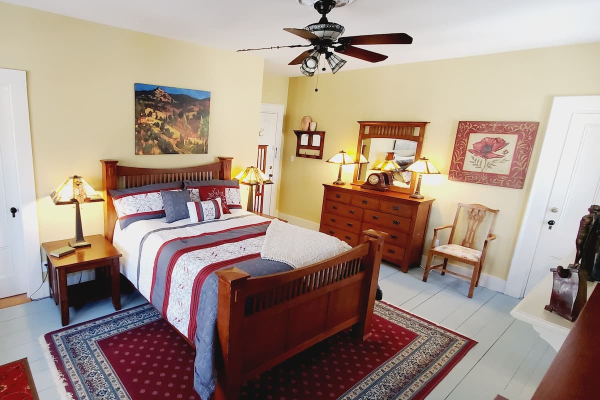 A bedroom with a wooden bed, bedside tables with lamps, a chair, a dresser, and a ceiling fan.