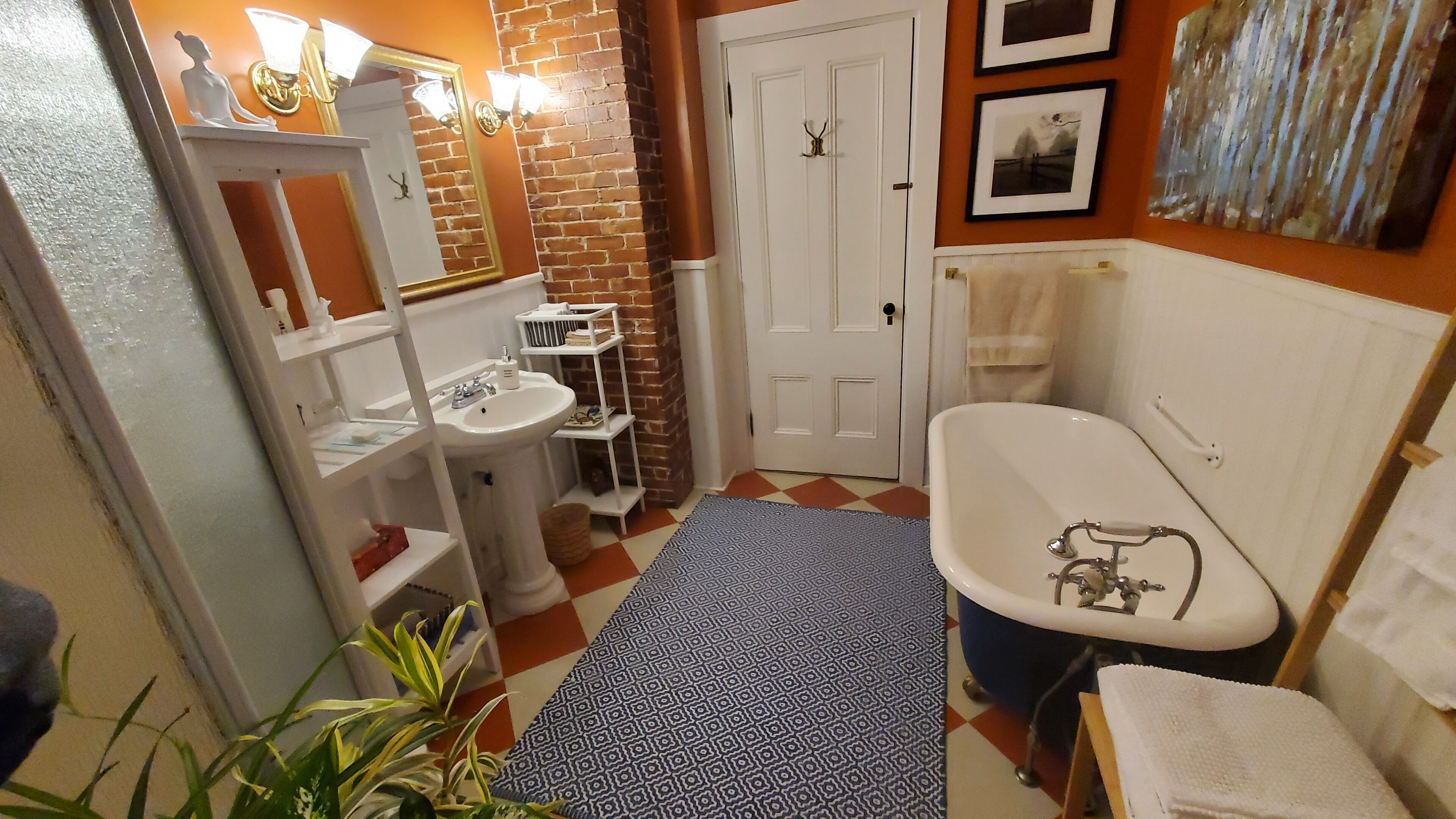 A bathroom with a white sink, a white toilet, a white bathtub, and a white door. There is a patterned rug on the floor and a plant in the corner.