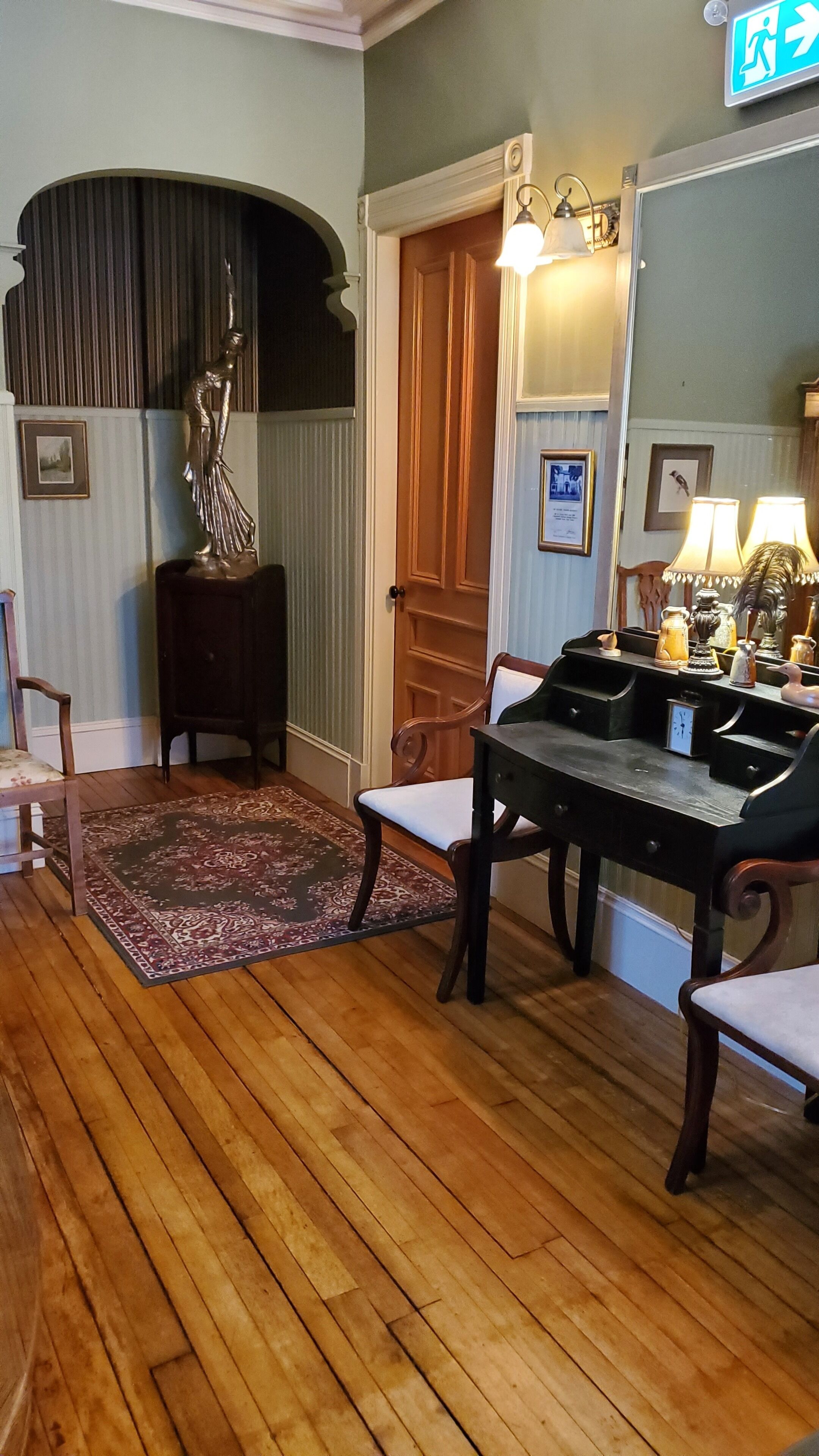 Una habitación con piso de madera, una mesa de comedor con sillas, una estatua, una puerta y una lámpara fijada a la pared.