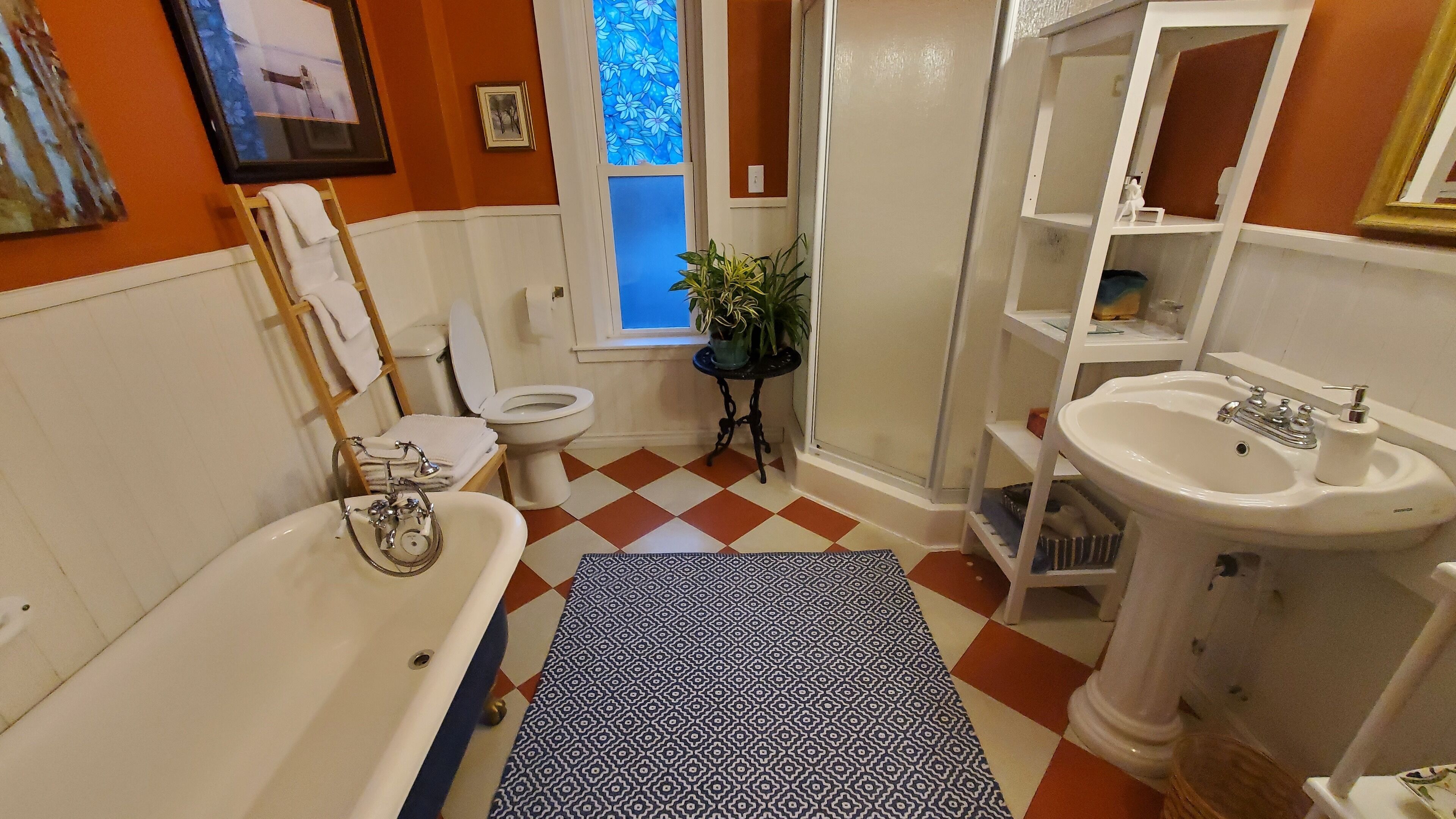 A bathroom with a white bathtub, a sink, a toilet, and a window with blue floral curtains.
