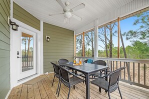 A covered outdoor patio with a table and chairs, a ceiling fan, and a view of trees.