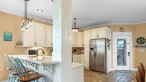 A kitchen with white cabinets, a stainless steel refrigerator, and a dining area with wooden chairs.
